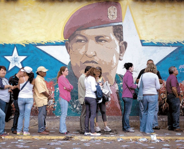 차베스의 얼굴 앞에 배급을 받기 위해 길게 늘어선 베네수엘라 시민들. 사회주의경제는 베네수엘라를 절망적으로 만들었다.